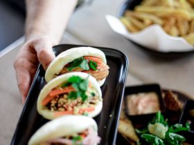 three bao buns on black oblong plate being held in air
