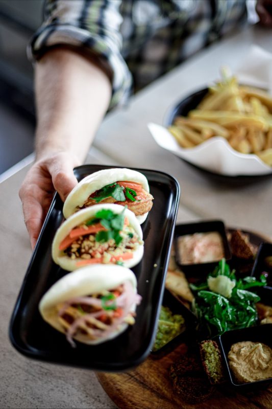 three bao buns on black oblong plate being held in air