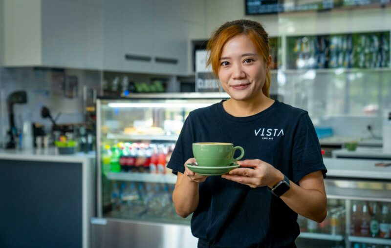 staff member holding a cup of coffee in a green cup