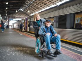 Travellers Aid volunteer assisting older man in wheelchair on Ballarat Station platform.