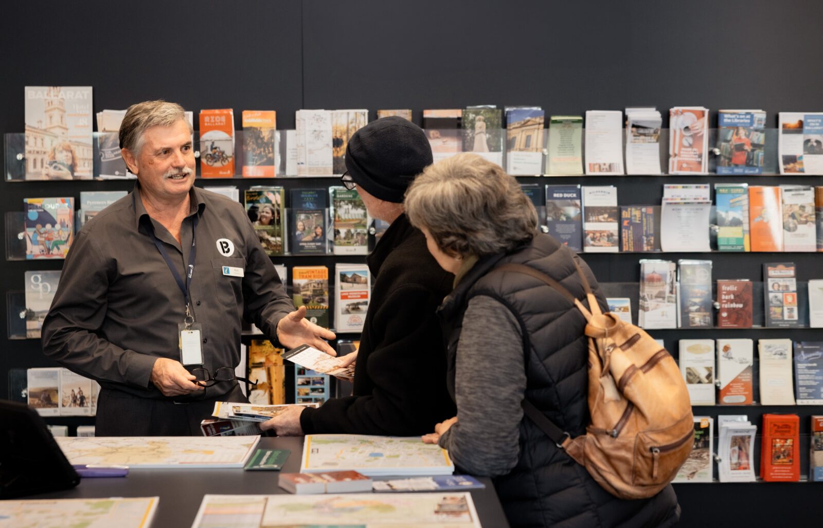 Rick standing in front of a brochure wall, helping two visitors