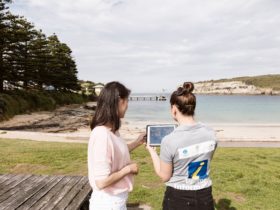 Visitor being shown information on a tablet on the Port Campbell foreshore