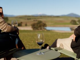 A glass of wine with two people on either side, with Mt Buller in the background