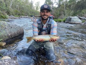 Nathan Vernon with large trout posing among rocks in a river