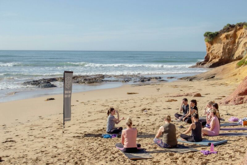 Eight participants doing a yoga class on the beach with the ocean and cliffs in the background