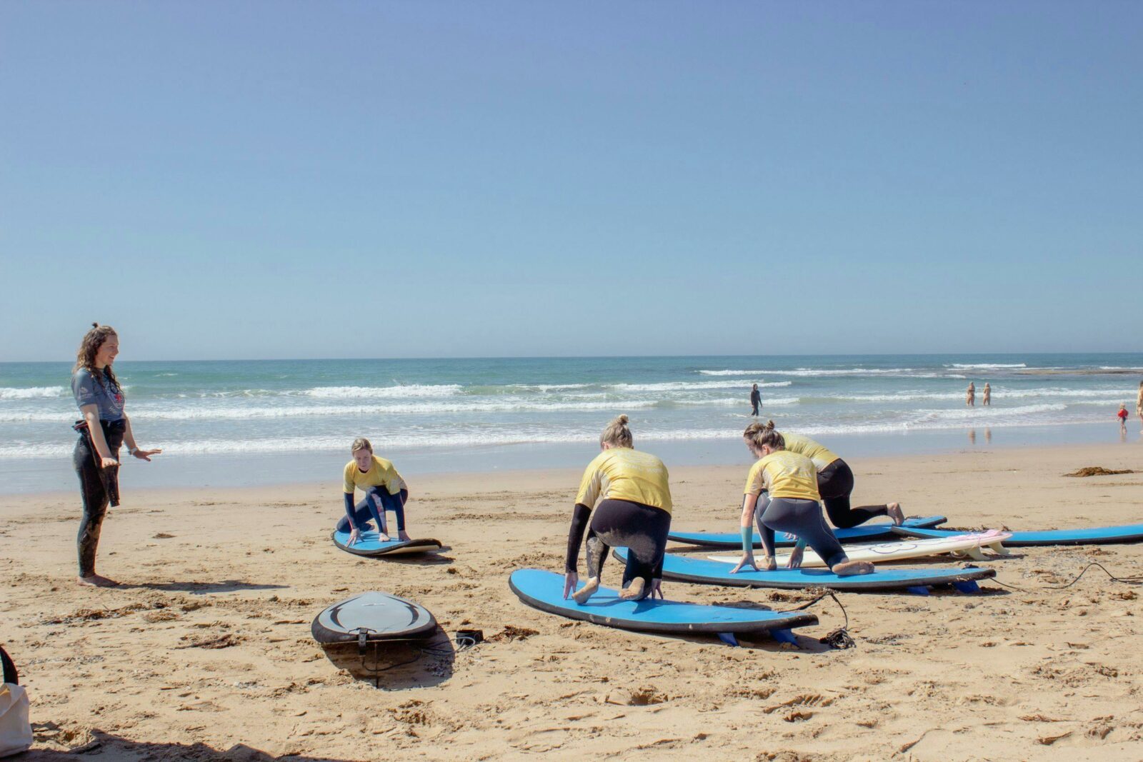 Four surfers practicing standing on boards on the sand with the surf instructor providing direction.