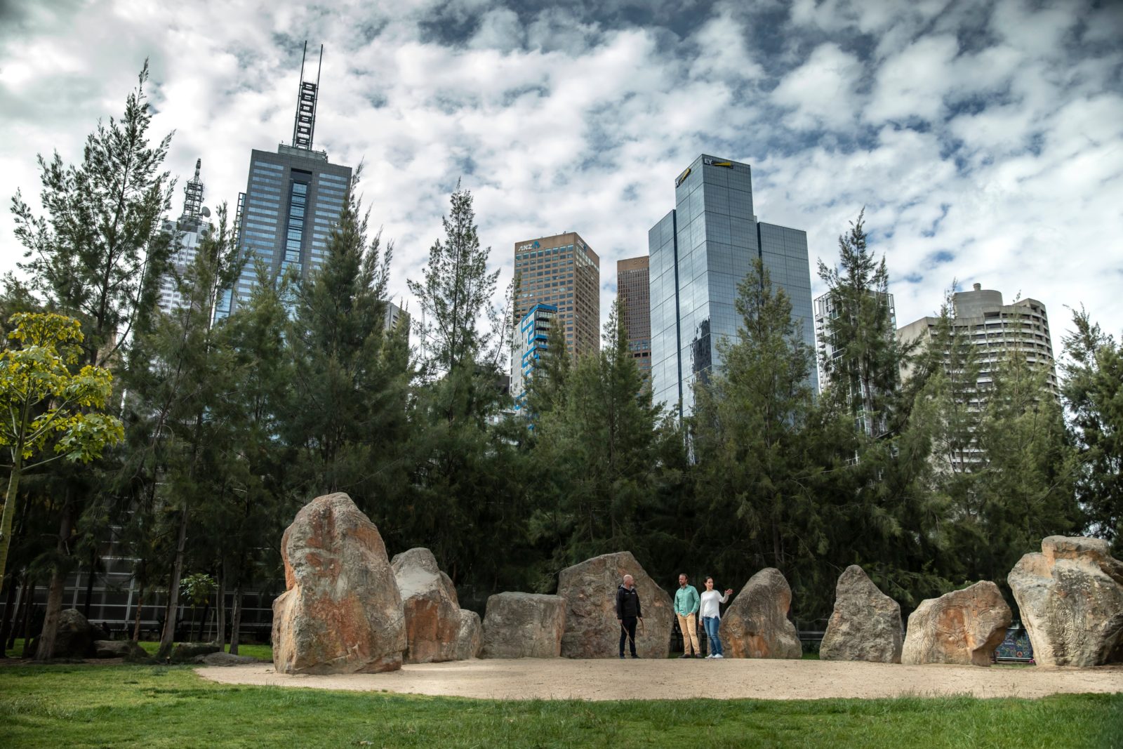 A group of people standing in a park with large rocks and trees.
