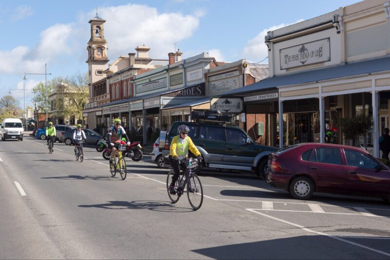 four cyclists riding beside historic shop fronts