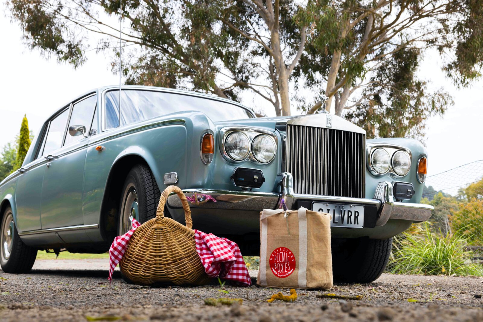A silver-blue 1974 Rolls Royce with picnic baskets in front of the car
