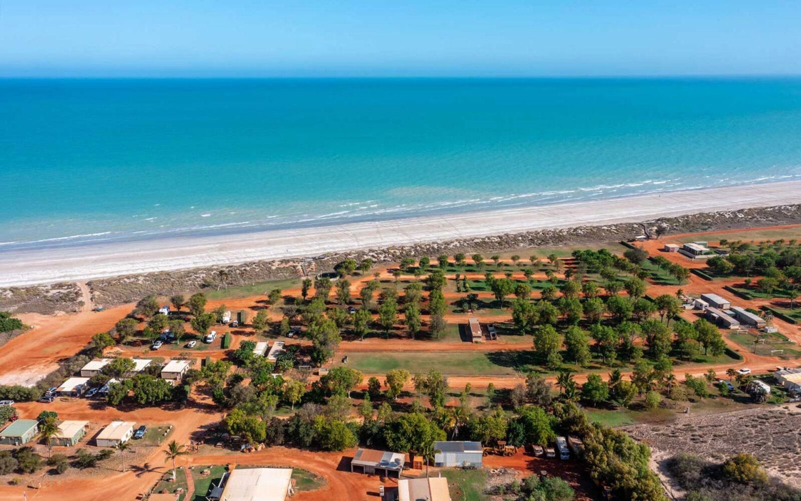 An aerial photo of a caravan park next to a stretch of pristine beach