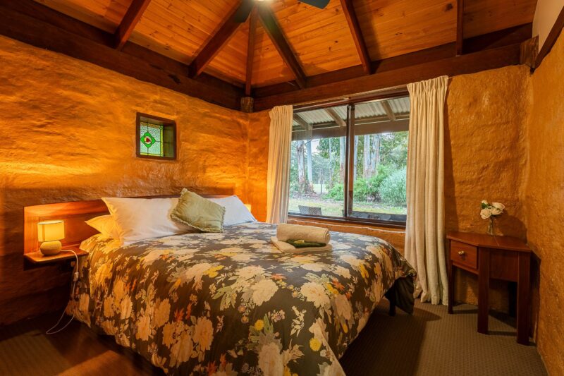 A queen sized bed with bedside lamps on the nightstands, a sunny outlook, raked ceiling s