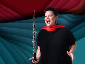 Liz Chee is smiling with her mouth open, balancing her oboe on the palm of her hand