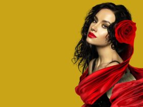 A woman with dark hair is featured against a gold backdrop. She wears a red rose in her hair.