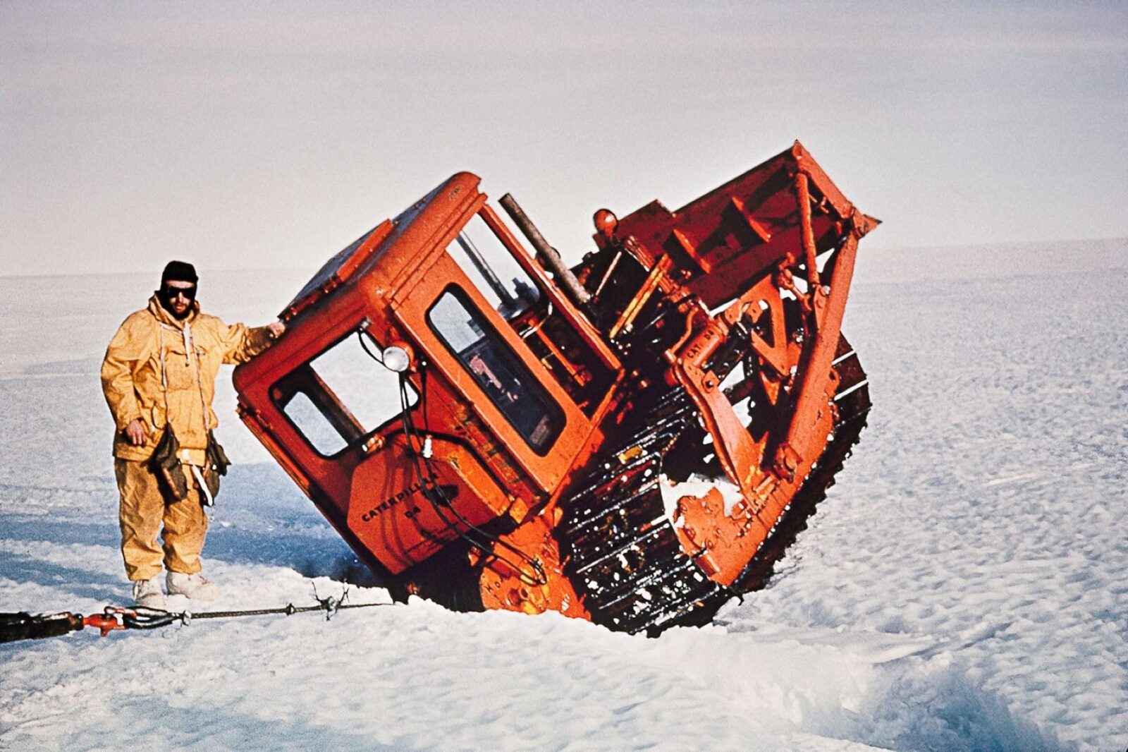 Man stands next to D5 tractor wedged in a crevice in Antarctica