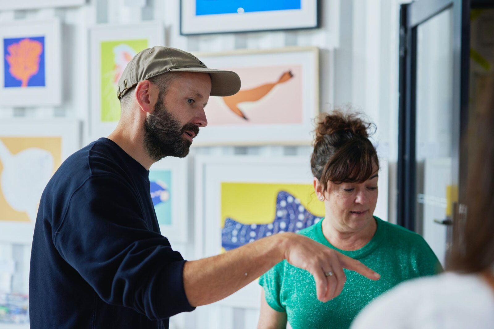Man with beard in cap showing a woman his artwork