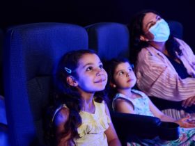 Two small girls and their mother watch the cinema experience, blue light filling the room