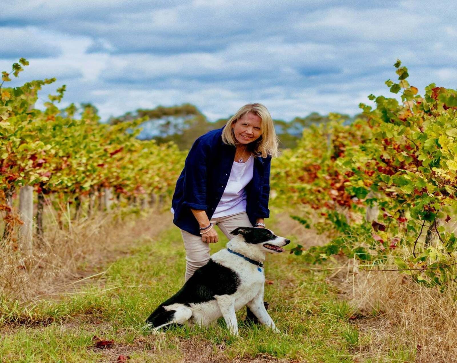 A lady in the Middle of wine field with a dog