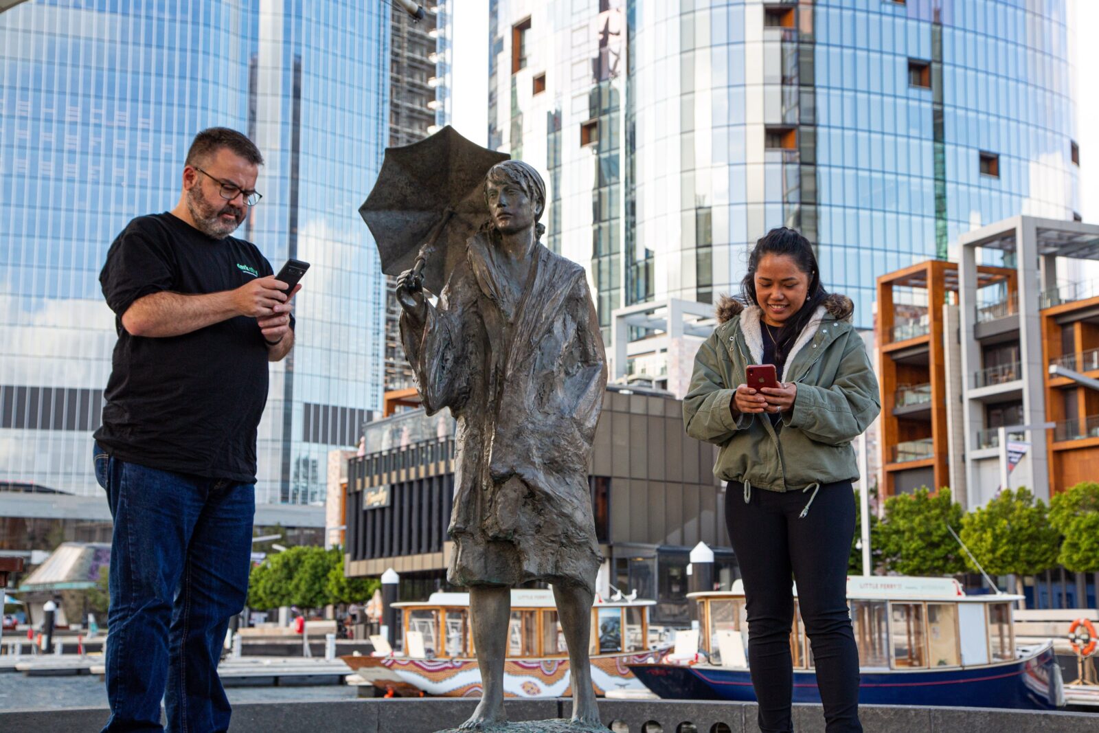 Two people looking at their phones next to a historical statue