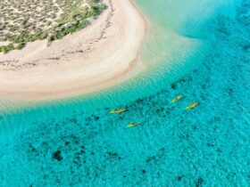 An aerial view of sea kayaks on turquoise water paddling around a white sandy point