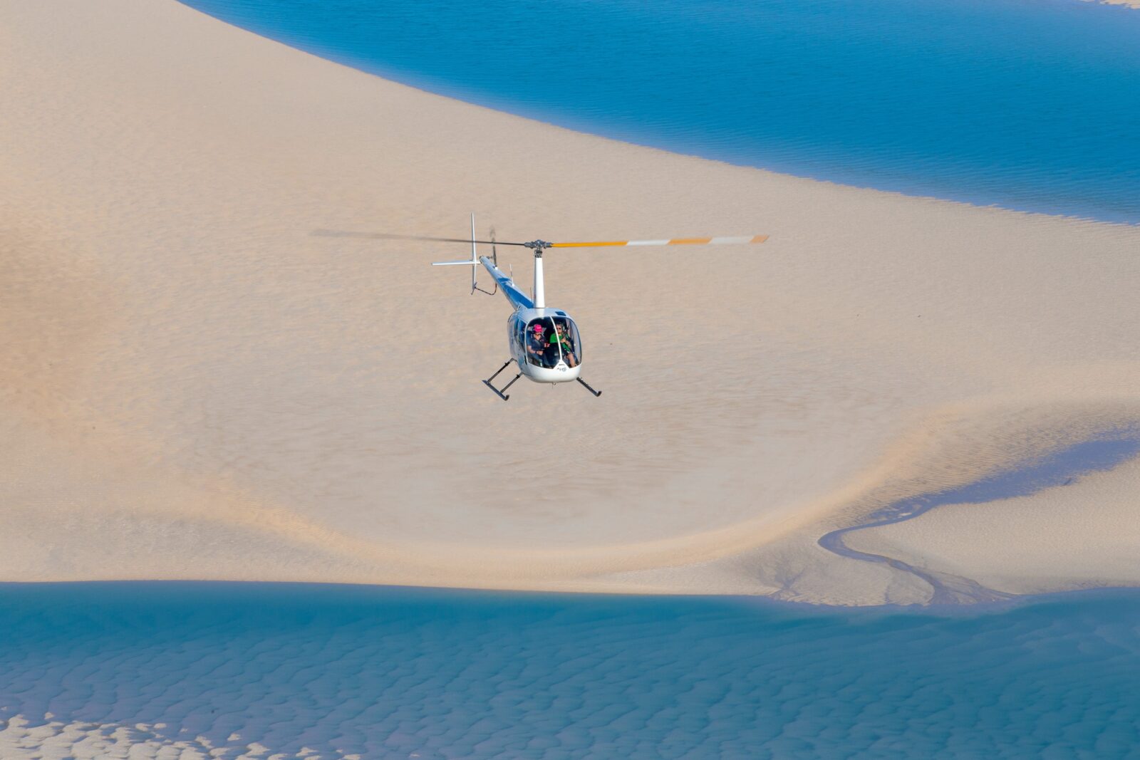 A helicopter flying over sandbars at low tide