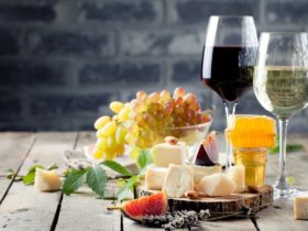 2 glasses of wine on a wooden table next to a plate of cheese and other condiments. red and white